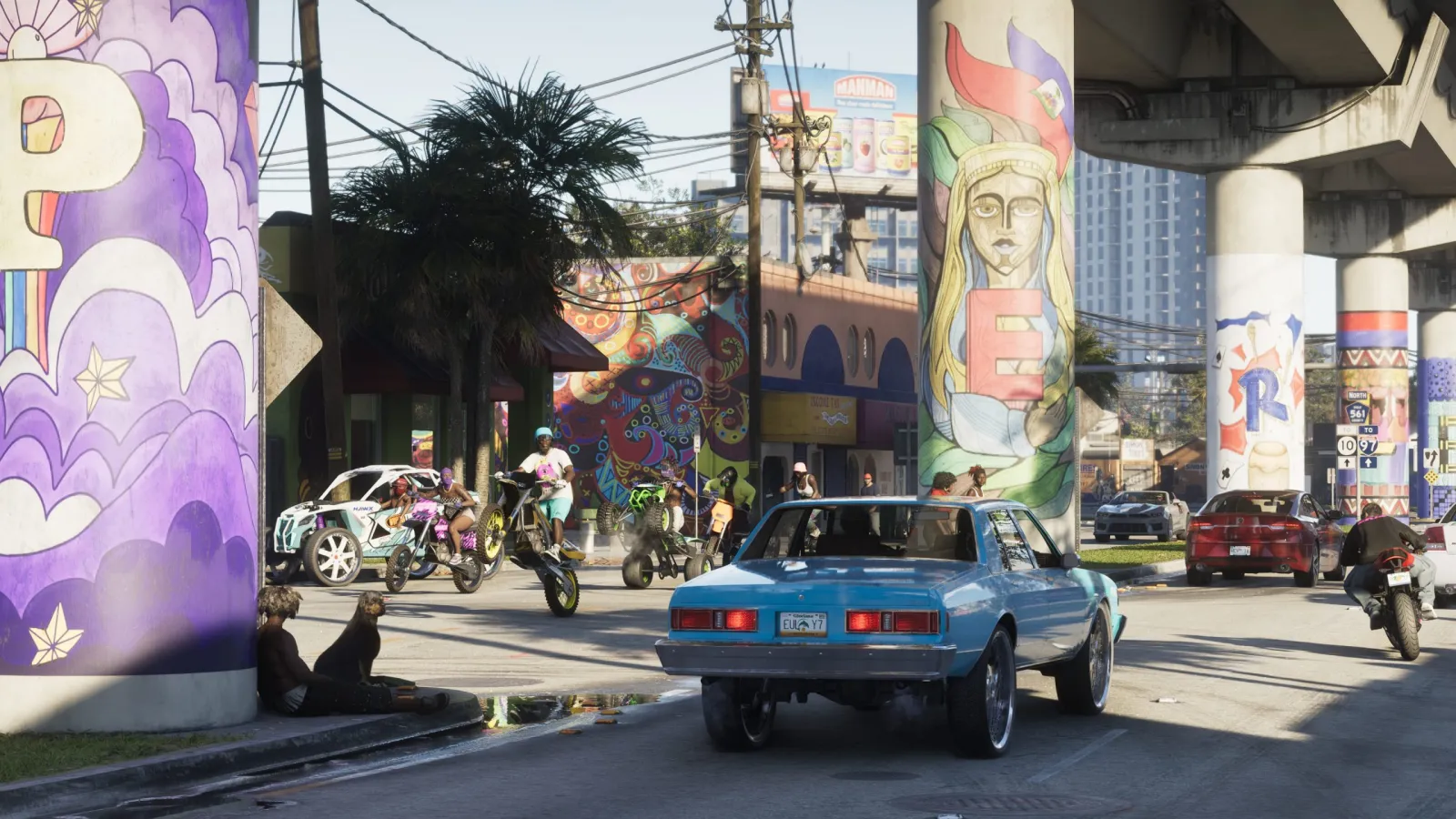 Un clásico muscle car azul en una calle de Vice City cubierta de murales en GTA 6, con motos y peatones alrededor